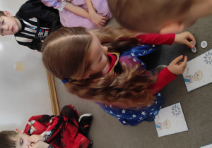 Dziewczynka układa liczmany- płatki śniegu obok ilustracji przedstawiającej Elzę, zgodniej z podanym na ilustracji działaniem.