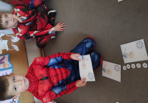 Chłopiec siedzący na dywanie trzyma w dłoniach wybraną przez siebie ilustrację przedstawiającą Elzę i działanie matematyczne.