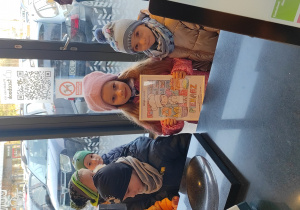 Dwie dziewczynki pozują do zdjęcia z upominkiem- pokolorowanym przez dzieci obrazkiem - przygotowanym dla pani sprzedającej w sklepie.