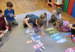 Dzieci siedzą na dywanie, chłopiec układa kredki wg kodu.