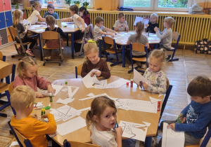 Dzieci siedzą przy stolikach, wycinają kredki.