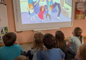 Dzieci oglądają na tablicy multimedialnej film dotyczący kolejnej postaci poznanej w projekcie.