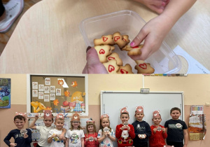 Dzieci pozują do wspólnego zdjęcia w opaskach i z pamiątkowymi odznakami i zajadają ciasteczka