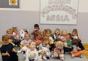 Dzieci z grupy Biedronki siedzą na dywanie i pozują do zdjęcia z przyniesionymi pluszowymi misiami.