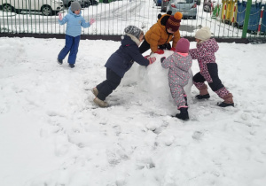 Dzieci lepią dużą śniegową kule.