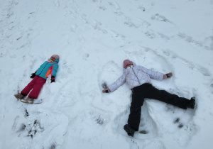 Dziewczynki leżą na śniegu, robią ,,aniołki”.