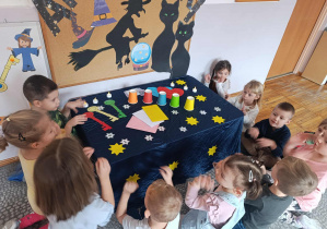 Dzieci stoją wokół stołu na którym przygotowane są wróżby dla nich.