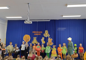 Zdjęcie przedstawia dzieci przebrane za różne owoce, warzywa i zwierzęta, a jedna z dziewczynek przebrana za jaskółkę deklamuje swój wierszyk.