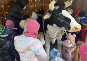 Dzieci stoją wokół plastikowej krowy.