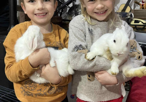 Dziewczynka i chłopiec pozują do zdjęcia trzymając króliki w rękach.