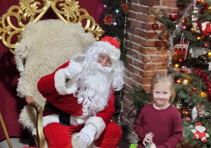 Dziewczynka pozuje do zdjęcia ze Świętym Mikołajem.