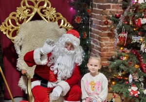 Dziewczynka pozuje do zdjęcia ze Świętym Mikołajem.