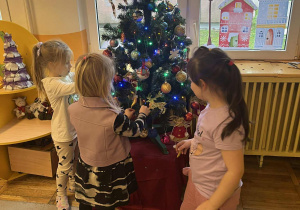 Dziewczynki zawieszają świąteczne ozdoby na choince.