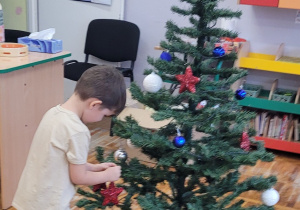 Dziewczynka wiesza bombkę na choince.