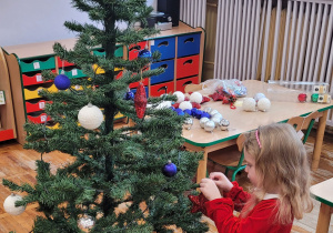 Dziewczynka wiesza bombkę na choince.