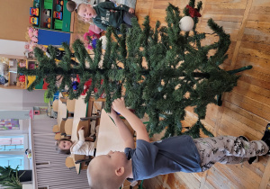 Chłopiec wiesza bombkę na choince.