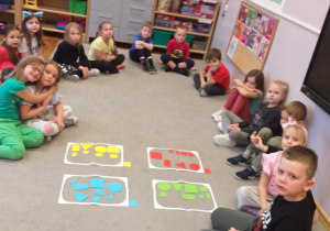 Zdjęcie przedstawia dzieci po posegregowaniu figur geometrycznych ze względu na kolor.