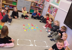 Zdjęcie przedstawia dzieci przed segregowaniem figur geometrycznych ze względu na wielkość.