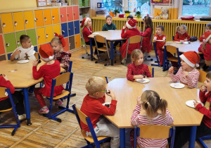 Dzieci siedzą przy stolikach, jedzą ciasto czekoladowe.