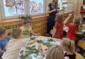 Zdjęcie przedstawia dzieci siedzące przy dwóch stolikach wykonujące swoje stroiki