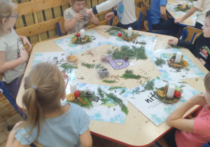 Zdjęcie przedstawia dzieci siedzące przy stolikach wykonujące swoje stroiki oraz już niektóre gotowe