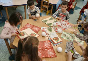 Dzieci zdobią bombki świątecznymi serwetkami.