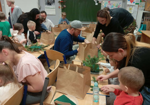 Zdjęcie przedstawia dzieci wraz z ich rodzicami wykonującymi stroik świąteczny.
