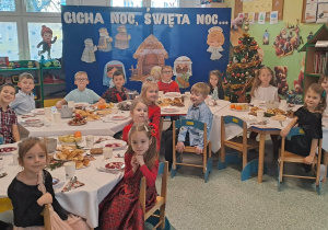 Grupowe zdjęcie przy stole z potrawami wigilijnymi.
