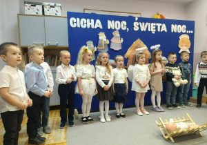 Dzieci stoją przed żłóbkiem śpiewając świąteczną piosenkę.