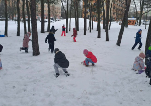 Dzieci biegają po śniegu i lepią śnieżki.
