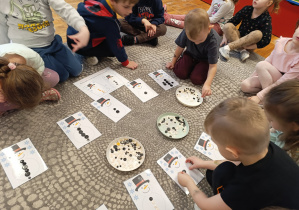 Dzieci układają bałwankom wskazaną ilość guzików.