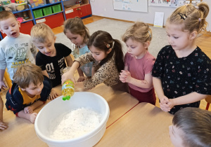 Dziewczynka dolewa do mąki olej.