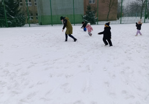 Dzieci biegają po śniegu i rzucają się śnieżkami.