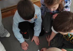 Dzieci siedzą na dywanie, przyglądają się ułożonej przez siebie matematycznej śnieżynce.