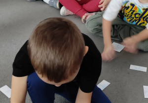 Chłopiec siedzący na dywanie dopasowuje do siebie ilustracje przedstawiające dwie połowy śnieżynki.