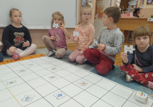 Na zdjęciu widzimy dzieci siedzące na dywanie pokazujące puzzle z literkami.