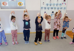 Dzieci stoją w rzędzie i trzymają papierowe kule nad głowami.
