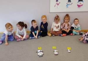 Przedszkolaki siedzą naprzeciw bałwanków ułożonych od najmniejszego do największego.