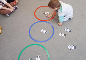 Przedszkolak kładzie bałwanka do obręczy w kolorze czerwonym.