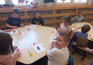 Zdjęcie przedstawia dzieci wyklejające kontur pingwina sztuką wydzieranki.