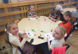 Zdjęcie przedstawia dzieci wyklejające kontur pingwina sztuką wydzieranki.