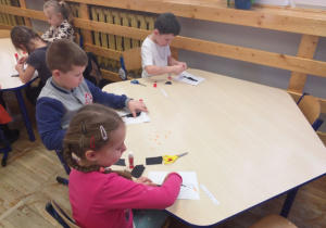 Zdjęcie przedstawia dzieci wyklejające kontur pingwina sztuką wydzieranki.