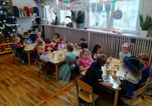 Dzieci siedzą przy stolikach.