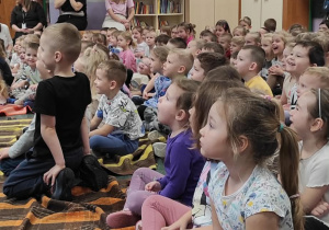 Dzieci siedzące na kocach z zaciekawieniem słuchają prezentowanej audycji muzycznej.