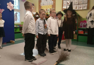 Chłopcy stoją na środku obok stoi dziewczynka przebrana za wiedźmę.