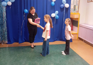 Pani wicedyrektor gratuluje dziewczynce i wręcza jej dyplom i nagrodę.