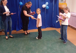 Pani wicedyrektor gratuluje dziewczynce i wręcza jej dyplom i nagrodę.