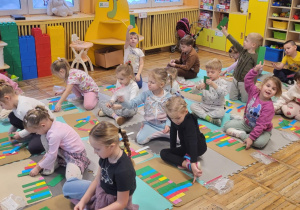 Dzieci siedzą na dywanie, układają klocki NEMI.