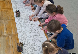 Dzieci wspólnie kolorują wielki arkusz papieru.