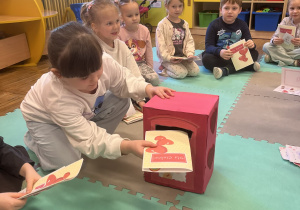 Dziewczynka wkłada kartkę walentynkową do skrzynki na listy.